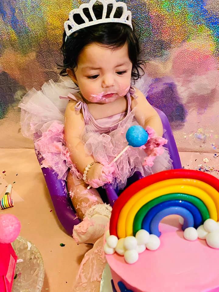 jenn pena's 6 month old tubal reversal baby girl eating a pink cake with rainbow decorations