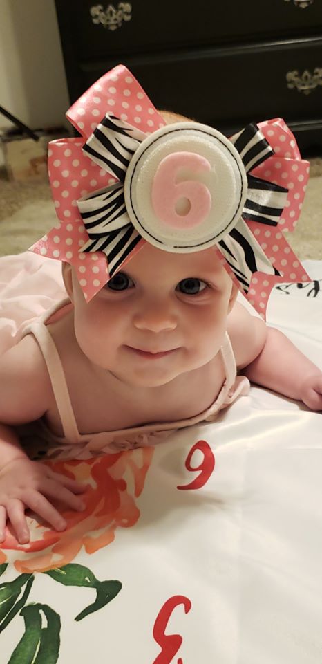 erica mosely's tr baby girl with a giant bow on her head indicating she is six months old