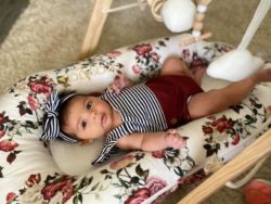 angela hurtado's tubal reversal baby is a girl laying on a floral sheet with a striped bow in her hair