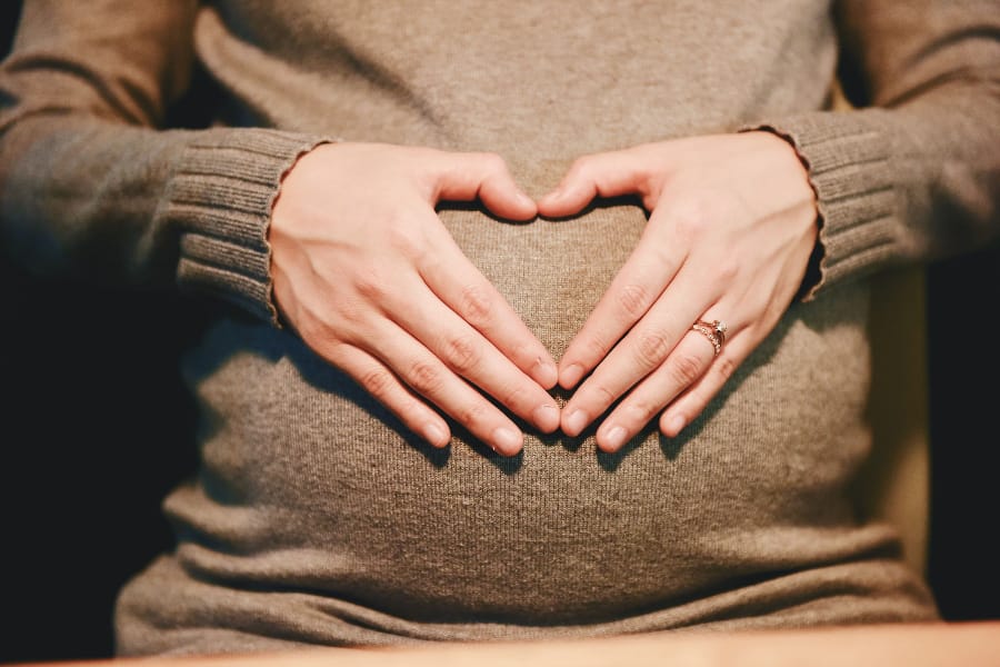 pregnant woman with hands over her baby belly with thumbs and fingers forming a heart