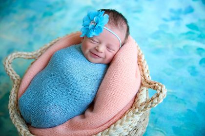 newborn picture of amanda fay albright' first tubal reversal baby girl swaddled in blue wearing a blue flower and placed in a basket