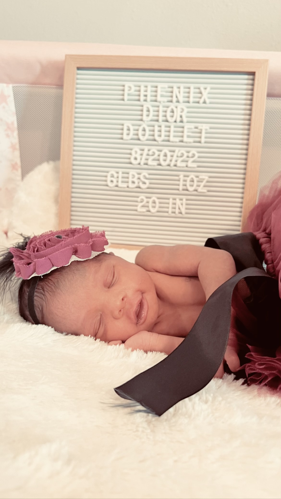 newborn tr baby girl named phenix sleeping with a birth announcement board behind her